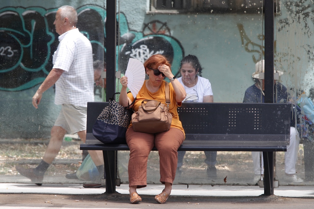 FILE - A woman tries to cool herself while waiting for a bus on a hot day in Skopje, North Macedonia, June 20, 2024. (AP Photo/Boris Grdanoski, File)