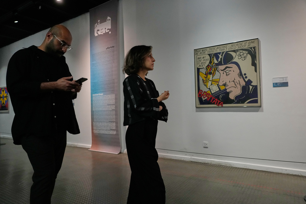 People visit an exhibition called: "Art & war" displaying some artworks of American pop artists as Roy Lichtenstein's "Brattata" is seen at right, at the Tehran Museum of Contemporary Art in Iran, Thursday, May 7, 2026. (AP Photo/Vahid Salemi)
