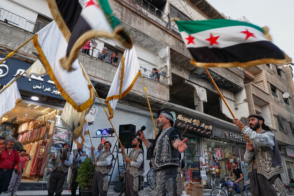 Residents watch a celebration below marking the opening of a new shop in the Damascus suburb of Daraya, Syria, Saturday, Oct. 4, 2025, ahead of a parliamentary election set to take place Sunday. (AP Photo/Omar Sanadiki)