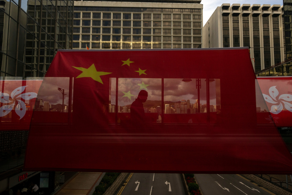 FILE- A pedestrian walks through a footbridge is silhouetted as Chinese and Hong Kong flags are strung to mark the 26th anniversary of the city's handover from Britain to China in Hong Kong, on June 27, 2023. (AP Photo/Louise Delmotte, File)