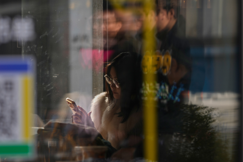 A woman looks at her smartphone in a cafe in Beijing, China, Thursday, Jan. 15, 2026. (AP Photo/Ng Han Guan)