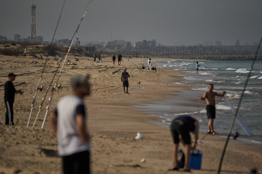 Backdropped by buildings destroyed during Israeli ground and air operations in the northern Gaza Strip, people walk and fish at Zikim Beach, near Ashkelon, in southern Israel, Friday, Oct. 17, 2025. (AP Photo/Leo Correa) Backdropped by buildings destroyed during Israeli ground and air operations in the northern Gaza Strip, people walk and fish at Zikim Beach, near Ashkelon, in southern Israel, Friday, Oct. 17, 2025. (AP Photo/Leo Correa)
