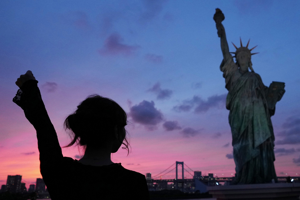A visitor mimics the position of the Statue of Liberty as she poses by the replica standing at Odaiba Seaside Park in Tokyo, Wednesday, June 17, 2026. (AP Photo/Hiro Komae)