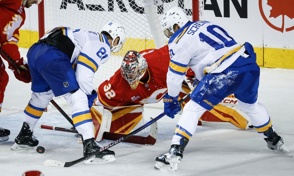 St. Louis Blues' Dylan Holloway, left, and Brayden Schenn, right, try to get the puck past Calgary Flames goalie Dustin Wolf during the third period of an NHL hockey game in Calgary, Alberta, Saturday, Oct. 11, 2025. (Jeff McIntosh/The Canadian Press via AP)