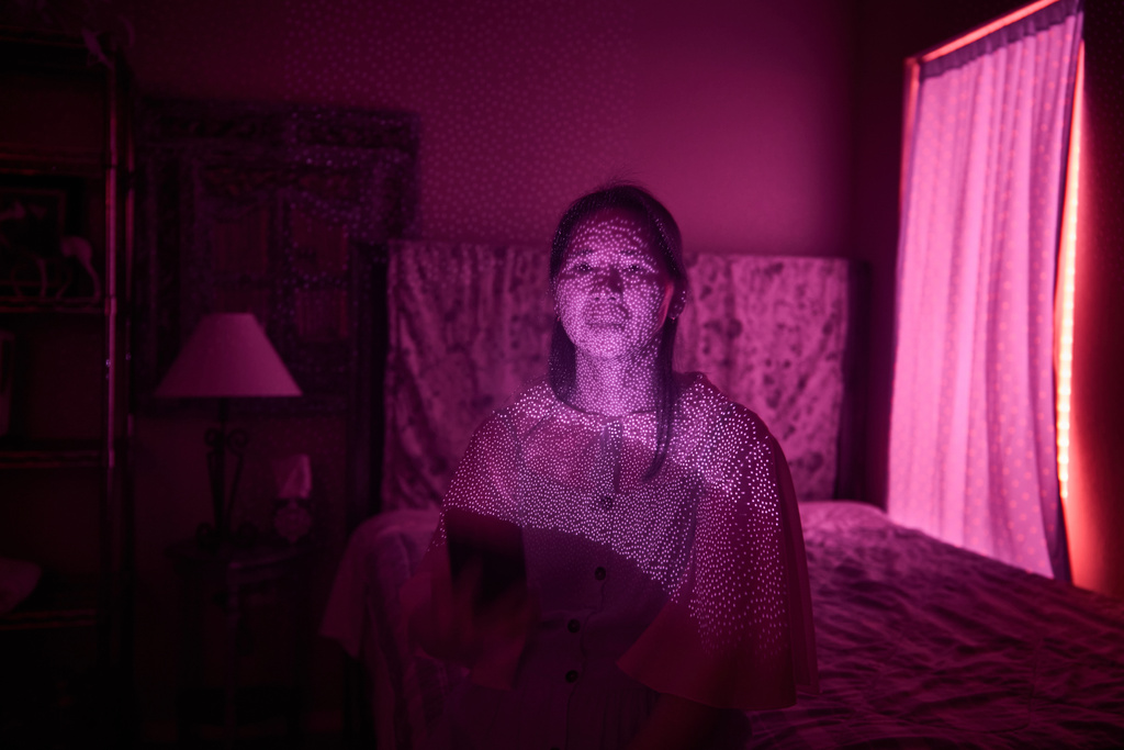 Dong e Li, a member of a Chinese church living in exile after fleeing from China, is illuminated by cellphone infrared facial recognition beams as she sits for a photo in her home, Oct. 13, 2025, in Midland, Texas. (AP Photo/David Goldman)