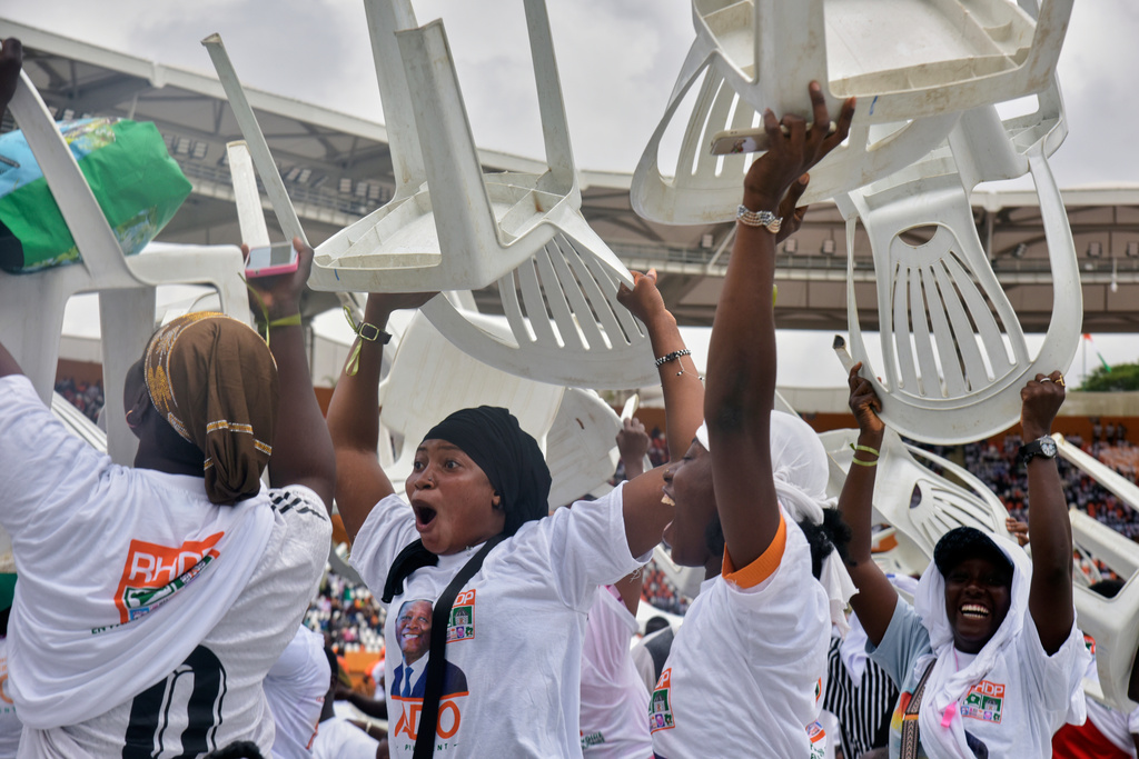 Supporters of President Alassane Ouattara lift plastic chairs and cheer during a campaign rally at the Félix Houphouët-Boigny Stadium in Abidjan, Ivory Coast, Saturday, Oct. 18, 2025. (AP Photo/Diomande Ble Blonde)
