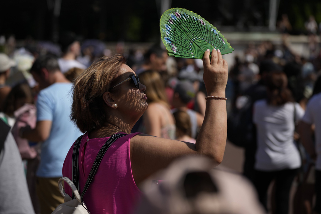 FILE - A tourist uses a fan to shade her face from the sun while waiting to watch the Changing of the Guard ceremony outside Buckingham Palace, during hot weather in London, July 18, 2022. (AP Photo/Matt Dunham, File)