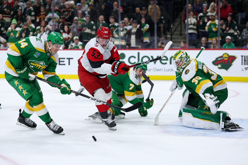 Carolina Hurricanes right wing Jackson Blake (53) and Minnesota Wild center Joel Eriksson Ek (14) compete for the puck as goaltender Jesper Wallstedt (30) defends his net during overtime of an NHL hockey game Wednesday, Nov. 19, 2025, in St. Paul, Minn. (AP Photo/Matt Krohn)