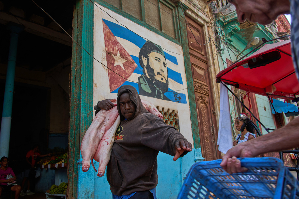 A man carries a pig at the entrance of a market, decorated with a mural of Fidel Castro, in Havana, Cuba, Wednesday, Aug. 12, 2026. (AP Photo/Ramon Espinosa)