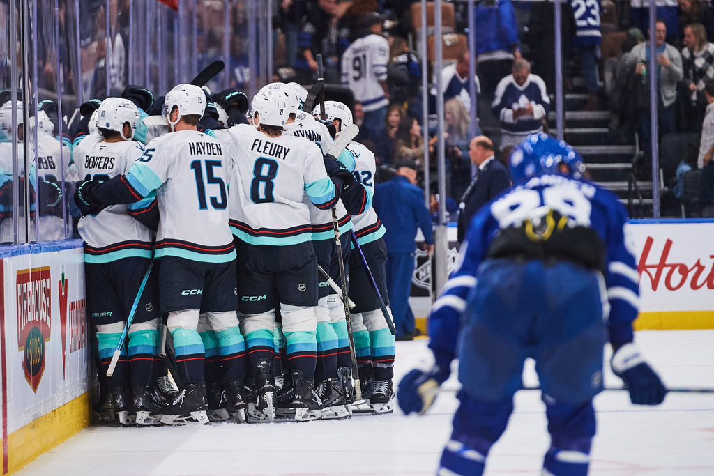 The Seattle Kraken celebrate Joshua Mahura's (28) game-winning goal as Toronto Maple Leafs' William Nylander (88) looks on during overtime in an NHL hockey game in Toronto on Saturday, Oct. 18, 2025. (Sammy Kogan/The Canadian Press via AP)