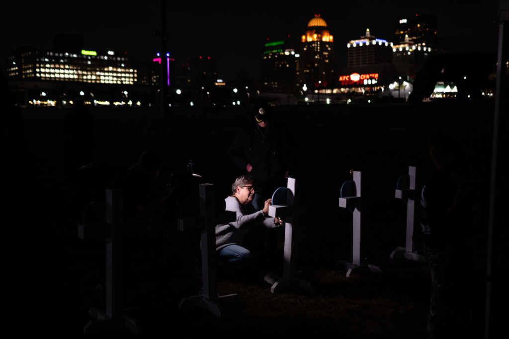 Dianne Graves writes on a heart-shaped placard attached to a cross during a vigil honoring the victims of a deadly UPS plane disaster, at the Great Lawn in Louisville, Ky., Friday, Nov. 7, 2025. (AP Photo/Jon Cherry)