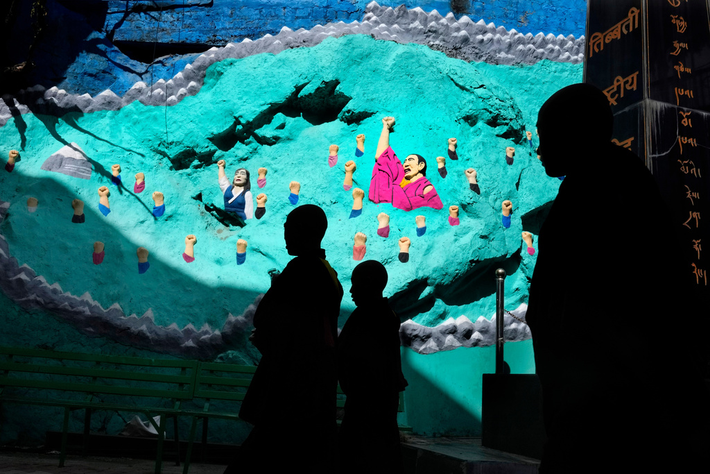 Tibetan monks are silhouetted as they walk past a mural at the Tsuglakhang temple in Mcleodganj near Dharamshala, India, March 6, 2025. (AP Photo/Manish Swarup)