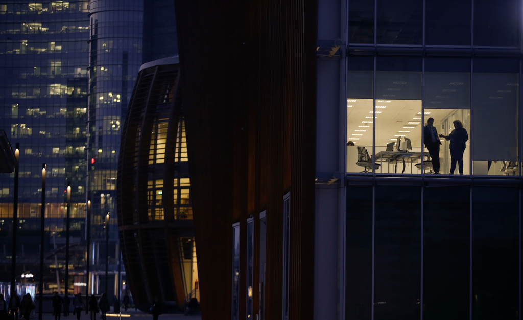 FILE - People are silhouetted behind the windows of an office, in Milan's Porta Nuova business district, Italy, on Oct. 18, 2017. (AP Photo/Luca Bruno, File)