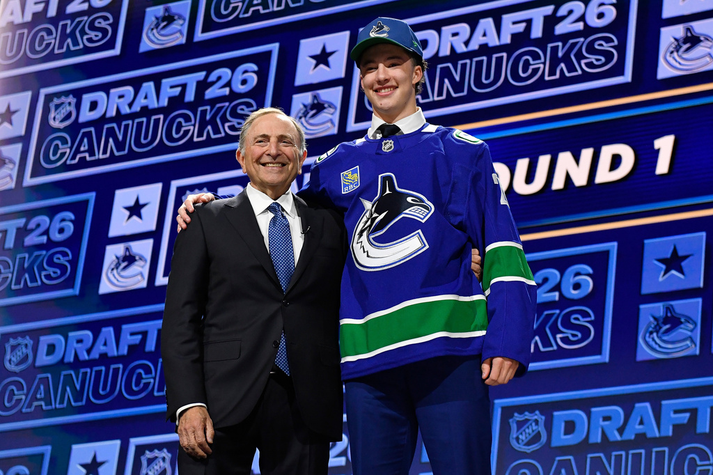 Caleb Malhotra, right, stands with NHL Commissioner Gary Bettman, left, after being drafted by the Vancouver Canucks during the NHL hockey draft Friday, June 26, 2026, in Buffalo, N.Y. (AP Photo/Adrian Kraus)