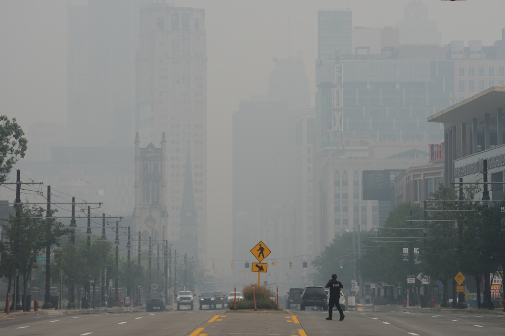 A pedestrian crosses the street as the Detroit city skyline is obscured during poor air quality due to smoke from Canadian wildfires Thursday, July 16, 2026, in Detroit. (AP Photo/Paul Sancya)