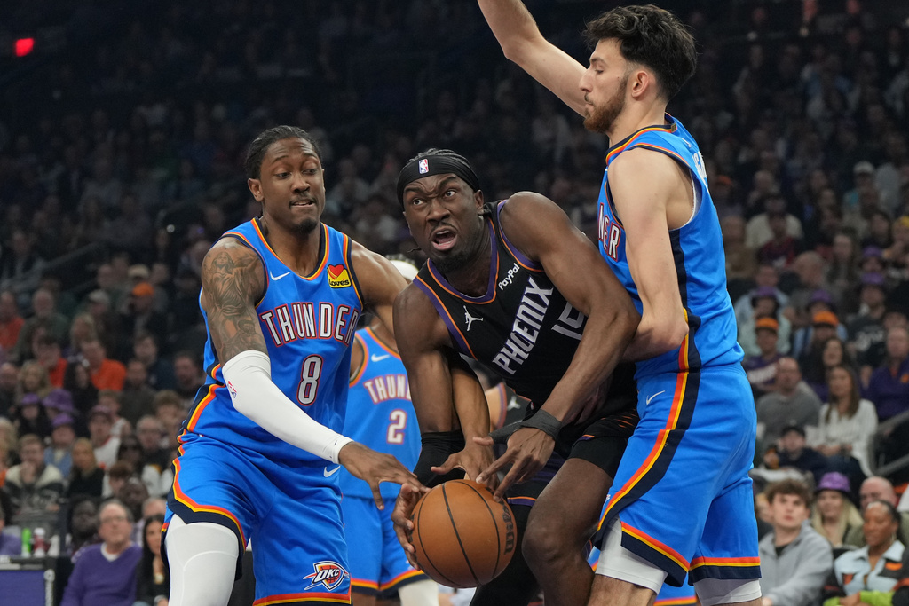 Phoenix Suns center Mark Williams drives between Oklahoma City Thunder guard Jalen Williams (8) and center Chet Holmgren during the first half of an NBA basketball game, Sunday, Jan. 4, 2026, in Phoenix. (AP Photo/Rick Scuteri)