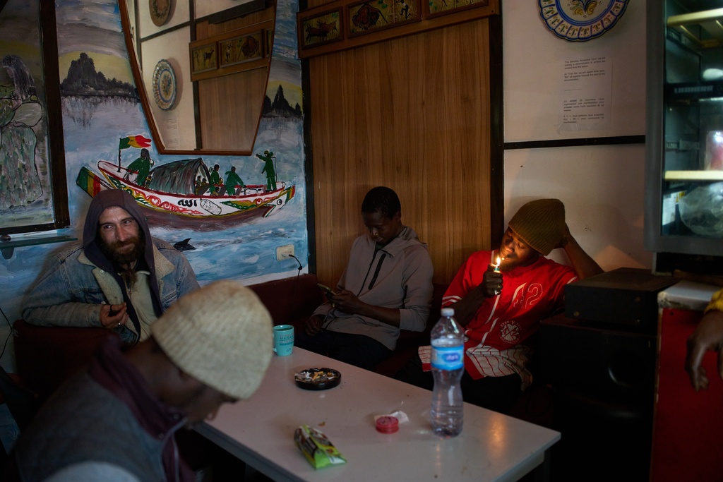 Migrants from Romania and Senegal sit in a makeshift bar inside an abandoned school in Badalona, near Barcelona, Spain, Monday, Dec. 15, 2025, where hundreds of migrants have been occupying the building. (AP Photo/Emilio Morenatti)