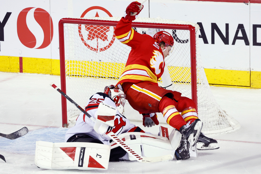 After a shot by Calgary Flames' Nazem Kadri (not shown) scores against New Jersey Devils goalie Jacob Markstrom, left, as Calgary Flames' Connor Zary, right, falls into the net during second-period NHL hockey game action in Calgary, Alberta, Monday, Jan. 19, 2026. (Larry MacDougal/The Canadian Press via AP)