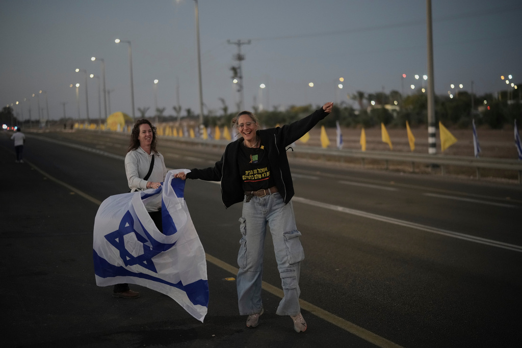 People wave Israeli flags as they gather prior to the release of Israeli hostages held in Gaza, in front of a military base near Reim Area, southern Israel, on Monday, Oct, 13, 2025. (AP Photo/Leo Correa)