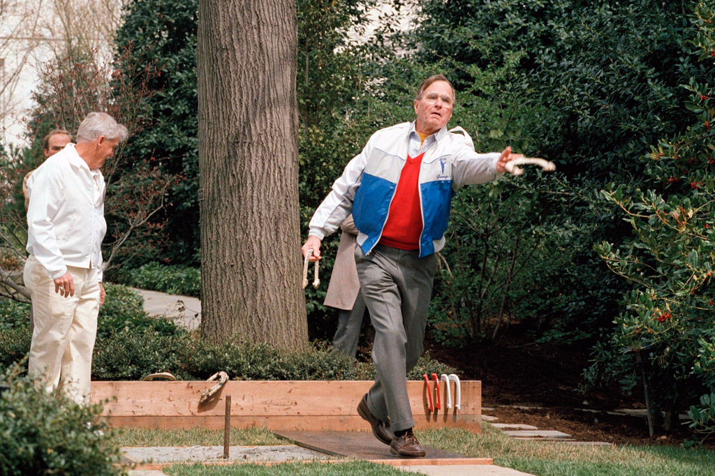 FILE - President George H.W. Bush lets loose of a horseshoe during the dedication of the new horseshoe pit on the White House lawn Saturday April 1, 1989, in Washington. (AP Photo/Barry Thumma)