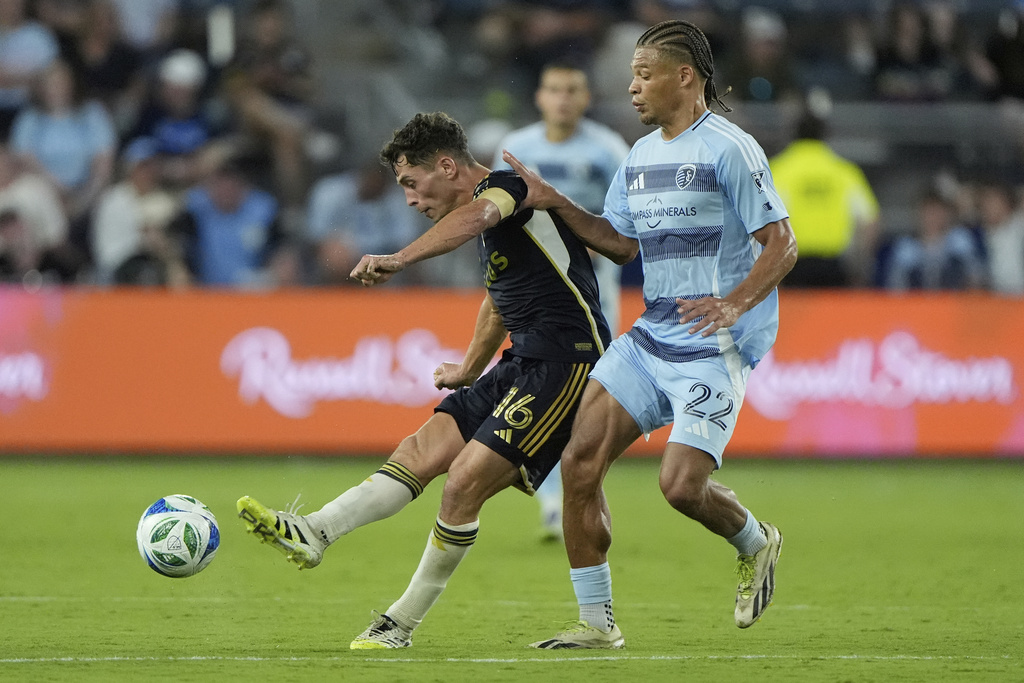 Vancouver Whitecaps midfielder Sebastian Berhalter (16) kicks the ball away from Sporting Kansas City midfielder Zorhan Bassong (22) during the second half of an MLS soccer match Saturday, Sept. 20, 2025, in Kansas City, Kan. (AP Photo/Charlie Riedel)