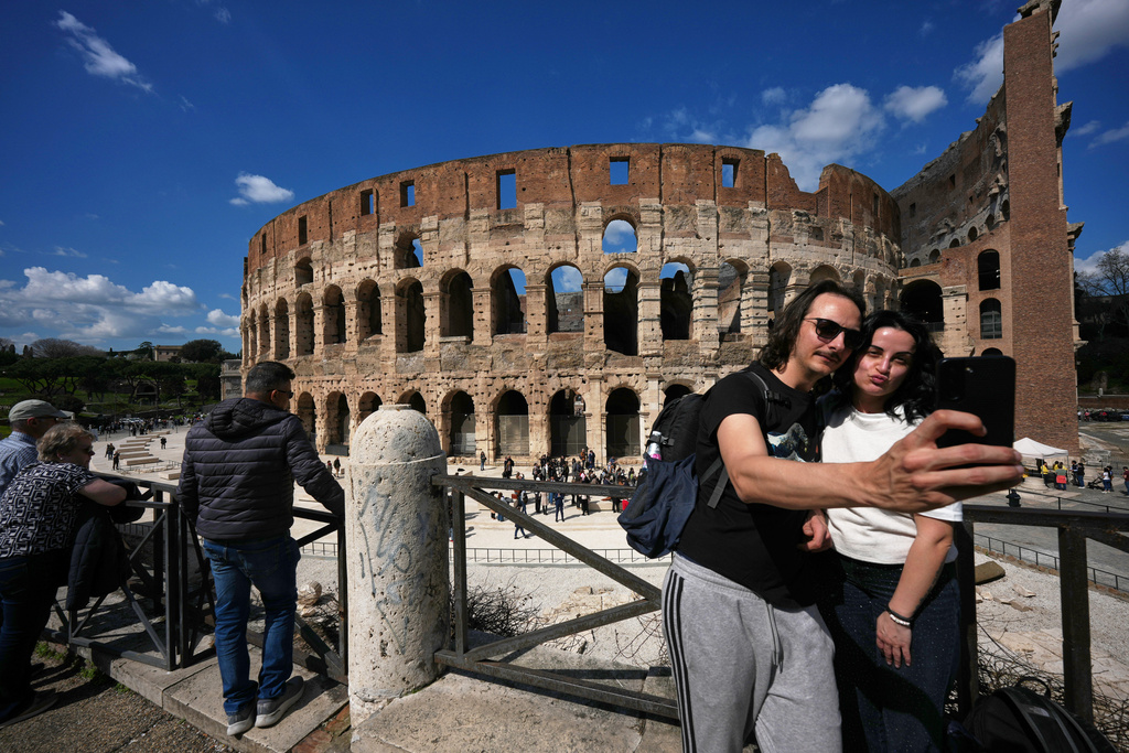 A couple take a selfie photo in front of the new outdoor space created with travertine marble around the Colosseum, during it's inauguration in Rome, Tuesday, March 17, 2026. (AP Photo/Andrew Medichini)