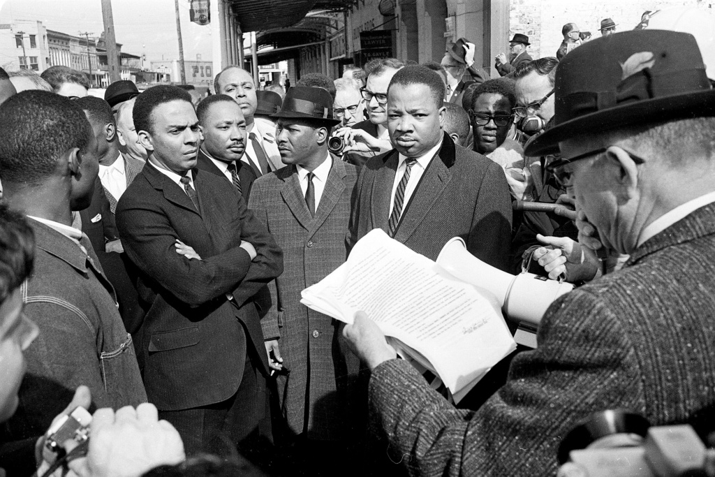FILE - A federal marshal reads a court order halting a planned voter registration protest as Dr. Martin Luther King Jr., right, and fellow marcher Andrew Young, left, look on in Selma, Ala., March 9, 1965. (AP Photo, File)