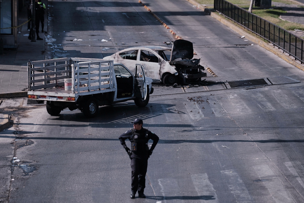 A police officer stands guard by a charred vehicle after it was set on fire, on a road in Guadalajara, Jalisco state, Mexico, Sunday, Feb. 22, 2026, after the death of the leader of the Jalisco New Generation Cartel, Nemesio Rubén Oseguera Cervantes, known as "El Mencho." (AP Photo/Alejandra Leyva)