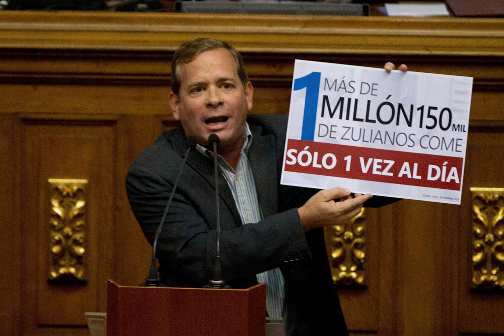 FILE - Opposition lawmaker Juan Pablo Guanipa displays a sign that reads in Spanish "More than a million residents of Zulia State eat only once a day" during an intervention against Venezuela's President Nicolas Maduro at National Assembly, in Caracas, Venezuela, Dec. 13, 2016. (AP Photo/Fernando Llano, File)