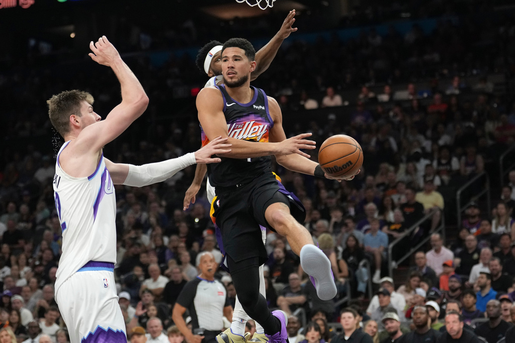 Phoenix Suns guard Devin Booker, right, looks to pass the ball against Utah Jazz forward Kyle Filipowski, left, during the first half of an NBA basketball game, Saturday, March 28, 2026, in Phoenix. (AP Photo/Ross D. Franklin)