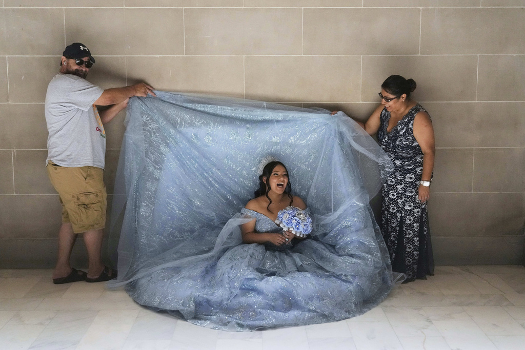 Abbie Gonzalez laughs as her mother Anna Gonzalez and mother's boyfriend William Umanzor lift her gown during her quinceañera portrait session at City Hall in San Francisco, Monday, Aug. 25, 2025. (AP Photo/Jeff Chiu)