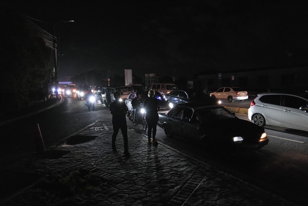 People watch as vehicles drive past during a blackout in Santo Domingo, Dominican Republic, Tuesday, Nov. 11, 2025. (AP Photo/Ricardo Hernandez)