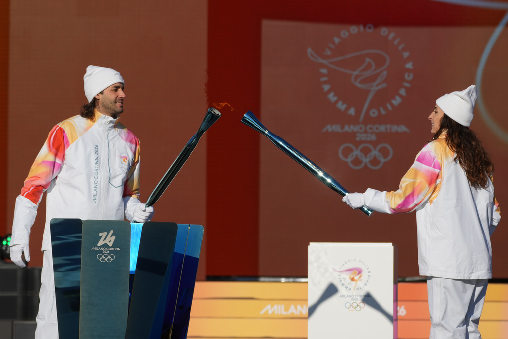 Italian high jumper and Olympic gold medalist Gianmarco Tamberi, left, receives the flame of the 2026 Milan Cortina Winter Olympics torch from Italian former foil fencer and Olympic and world champion Elisa Di Francisca in Rome as it begins its journey through Italy, Saturday, Dec. 6, 2025, a journey that will conclude in Milan in February 2026. (AP Photo/Andrew Medichini)