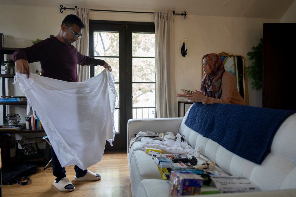 Faisal Rashid, left, practices putting on his ihram robe as he speaks with his wife Samiha Matin as they packfor the annual Hajj pilgrimage in Mecca, Saudi Arabia, at their home in Pasadena, Calif, Sunday, May 17, 2026. (AP Photo/Ryan Sun)