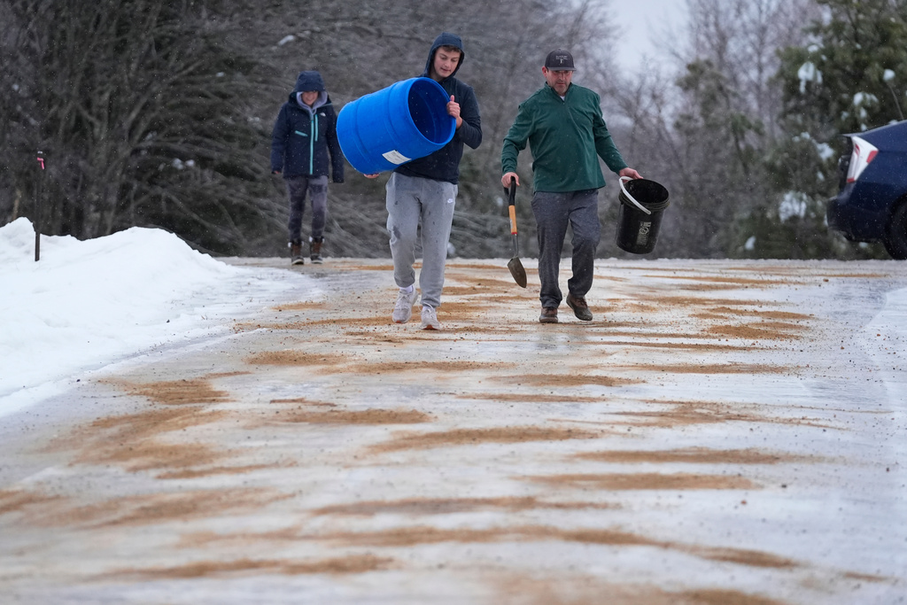 Chase Caruso, center, and his father, Peter Caruso, spread sand on their icy driveway during a freezing rainstorm, Monday, Dec. 29, 2025, in Harrison, Maine. (AP Photo/Robert F. Bukaty)