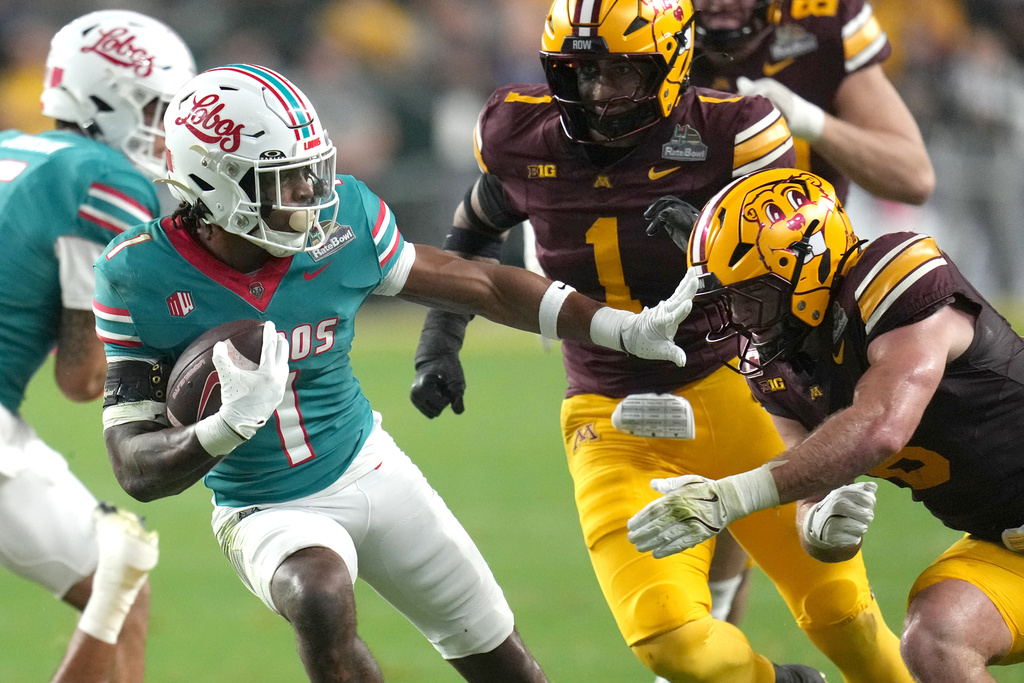 New Mexico running back Damon Bankston (1) stiff arms Minnesota defensive lineman Steven Curtis in the first half of a Rate Bowl NCAA college football game, Friday, Dec. 26, 2025, in Phoenix. (AP Photo/Rick Scuteri)