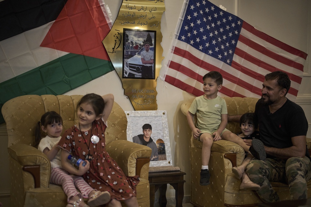 Mohammed Rabee, 48, sits with his grandchildren beside photos of his 14-year-old son, Amer Rabee, who was killed by Israeli soldiers while in a roadside thicket in the West Bank town of Turmus Ayya, April 22, 2025. (AP Photo/Leo Correa)