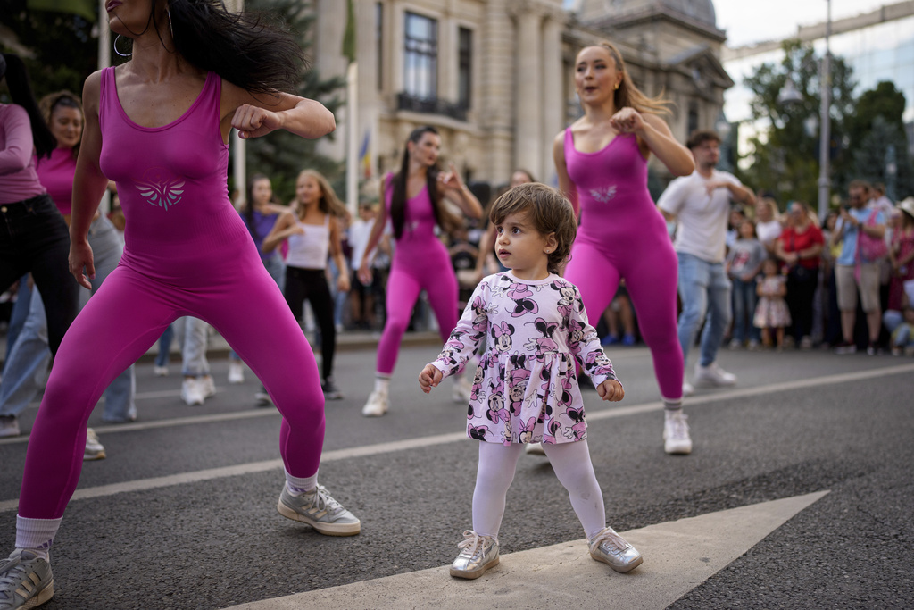 A child watches dancers perform outside the National History Museum of Romania during Dance Night, an event featuring a wide variety of dance styles performed on the Calea Victoriei avenue in Bucharest, Romania, Saturday, Aug. 23, 2025. (AP Photo/Andreea Alexandru)