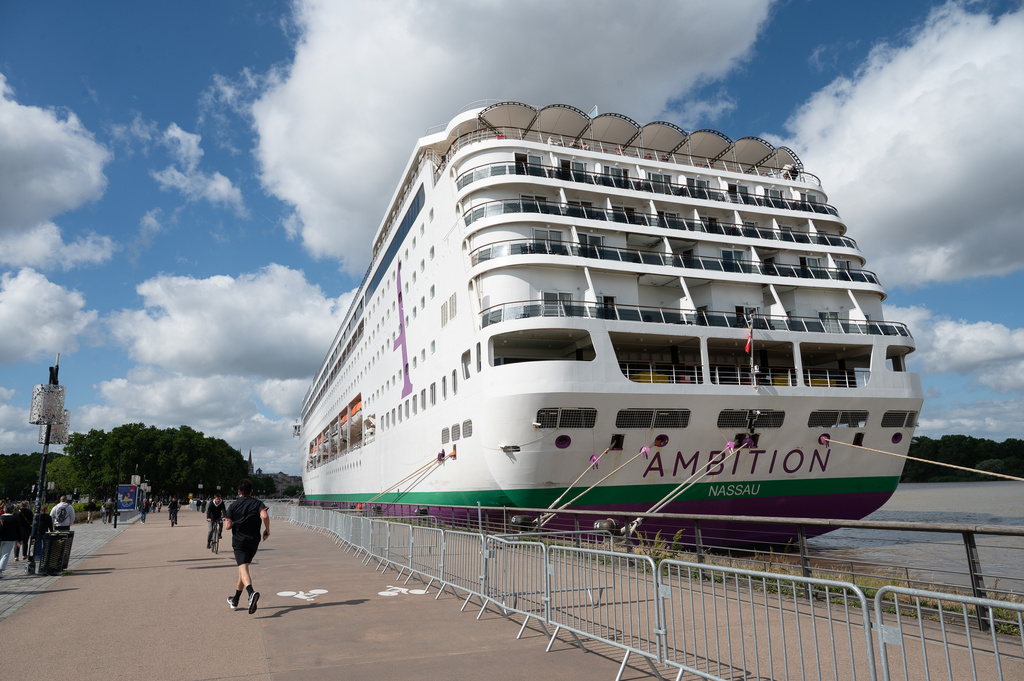 People walk past the British cruise ship Ambition, as French authorities have ordered 1,700 passengers and crew to stay on board due to a gastrointestinal illness outbreak, in Bordeaux, southwestern France, Wednesday, May 13, 2026. (AP Photo/Caroline Blumberg)