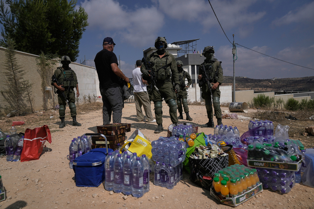 Activists accumulate food and water supplies in front of Israeli army soldiers who are blocking the road leading to the houses of three Palestinian families that have been besieged by Israeli settlers for six days, in the occupied West Bank village of Qusra, south of Nablus, Friday, Aug. 14, 2026. (AP Photo/Majdi Mohammed)