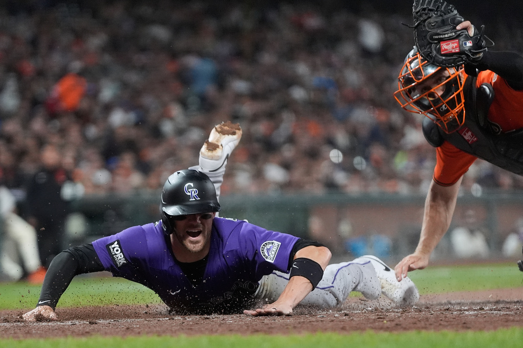 Colorado Rockies' Brett Sullivan, left, scores past San Francisco Giants catcher Andrew Knizner, right, during the fifth inning of a baseball game, Friday, Aug. 14, 2026, in San Francisco. (AP Photo/Jeff Chiu)
