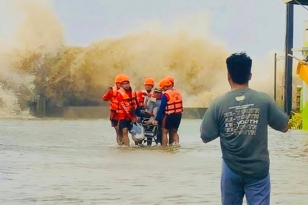 In this photo provided by the Philippine Coast Guard, rescuers evacuate a resident on a wheelchair as waves batter due to Tropical Storm Bualoi in San Agustin, Romblon province, Philippines on Friday Sept. 26, 2025. (Philippine Coast Guard via AP)