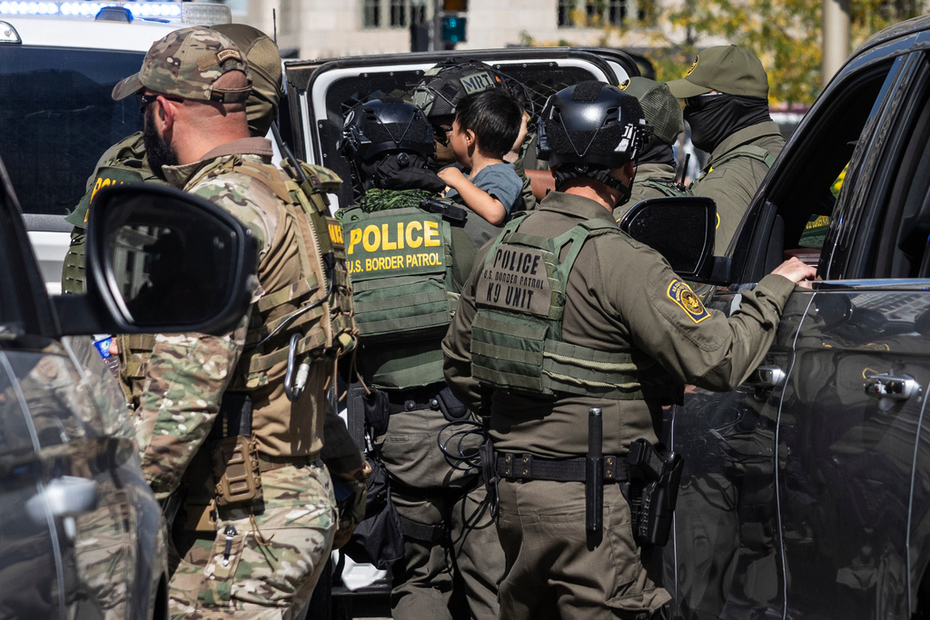 A federal agent carries a child as agents detain someone near Pioneer Court off the Magnificent Mile, Sunday, Sept. 28, 2025, in Chicago. (Ashlee Rezin/Chicago Sun-Times via AP)