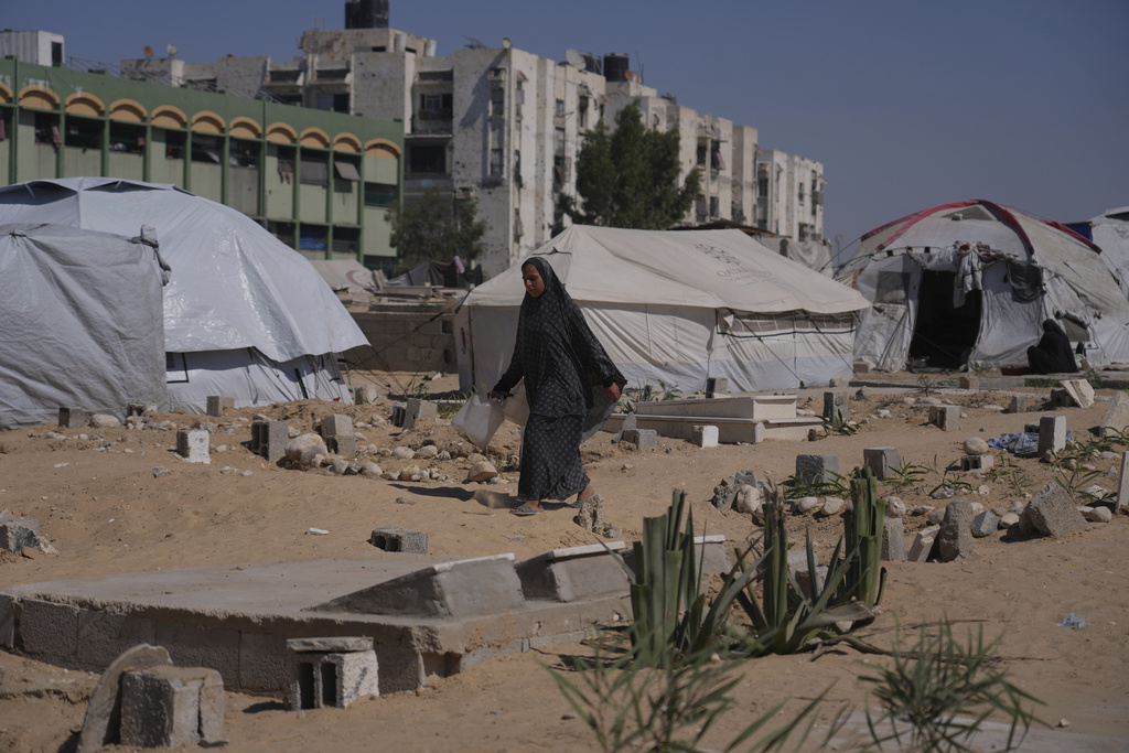 A displaced Palestinian woman walks past makeshift tents set up in a cemetery in Khan Younis, in the southern Gaza Strip, Saturday, Sept. 20, 2025. (AP Photo/Jehad Alshrafi)