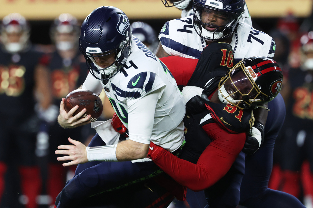 Seattle Seahawks quarterback Sam Darnold, left, is sacked by San Francisco 49ers defensive tackle Sam Okuayinonu (91) during the first half of an NFL football game in Santa Clara, Calif., Saturday, Jan. 3, 2026. (AP Photo/Jed Jacobsohn)
