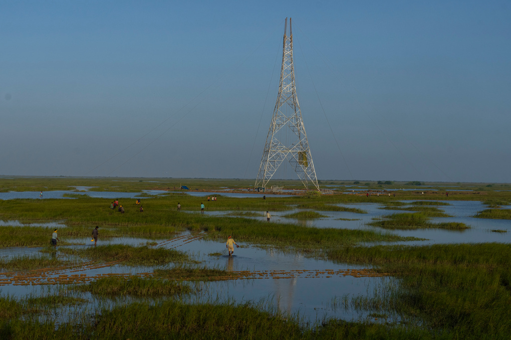FILE - Workers walk through a swamp to install electric transmission towers for the Adani Renewable Energy Park near Khavda, Bhuj district, near the India-Pakistan border in the western state of Gujarat, India, Sept. 21, 2023. (AP Photo/Rafiq Maqbool, File)