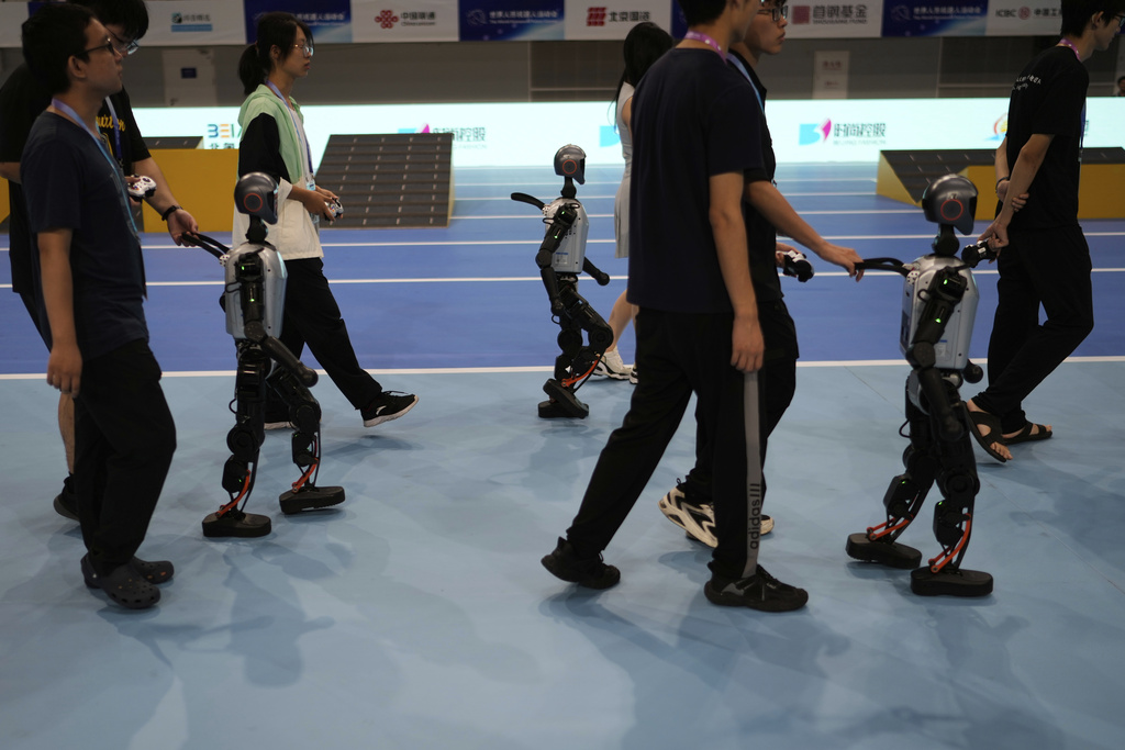 Technicians guide robots away after they competed in a soccer event at the World Humanoid Robot Games Beijing, China, Saturday, Aug. 16, 2025. (AP Photo/Mahesh Kumar A.)