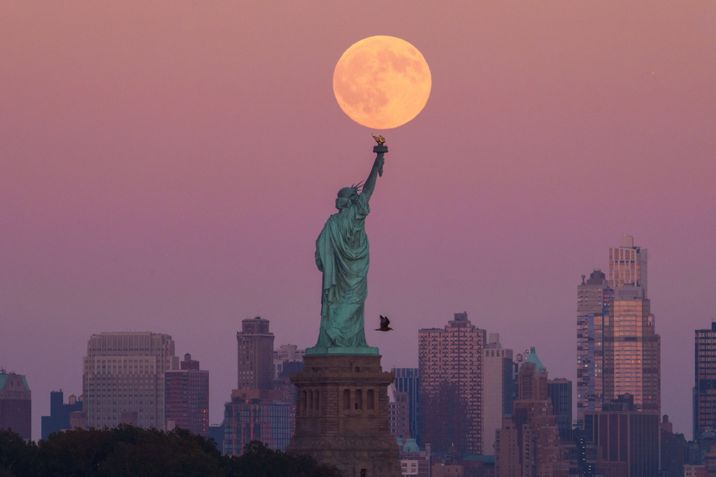 The Harvest Supermoon rises behind the Statue of Liberty and the Brooklyn skyline, Monday, Oct. 6, 2025, in Jersey City, N.J. (AP Photo/Adam Gray)