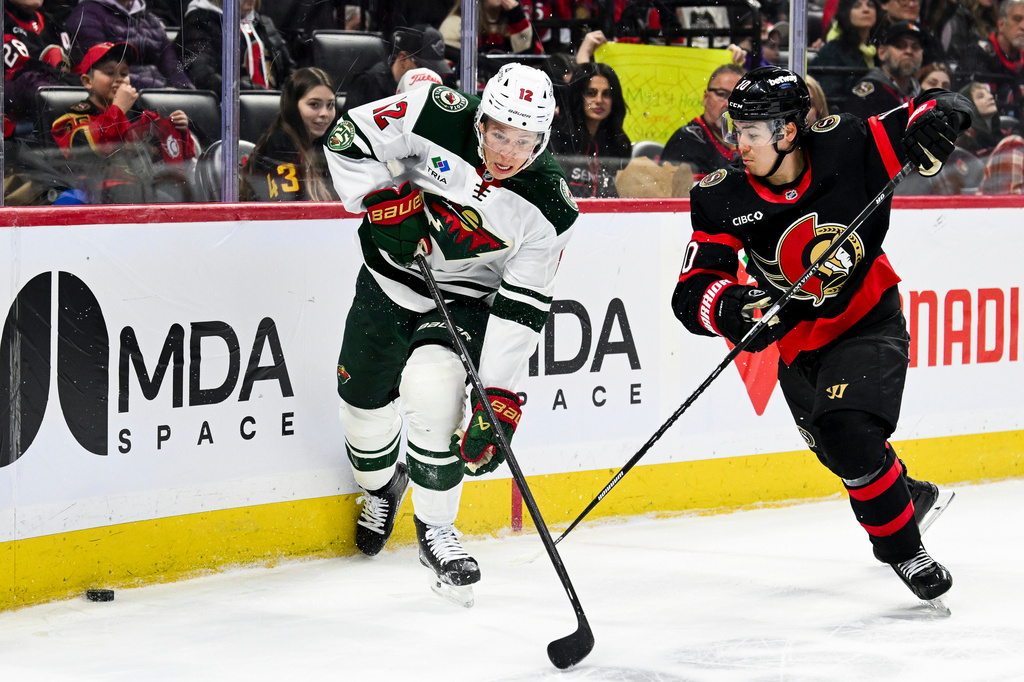 Minnesota Wild's Matt Boldy (12) and Ottawa Senators' Jordan Spence (10) fight for control of the puck along the boards during the first period of an NHL hockey game, Saturday, April 4, 2026, in Ottawa, Ontario. (Spencer Colby/The Canadian Press via AP)