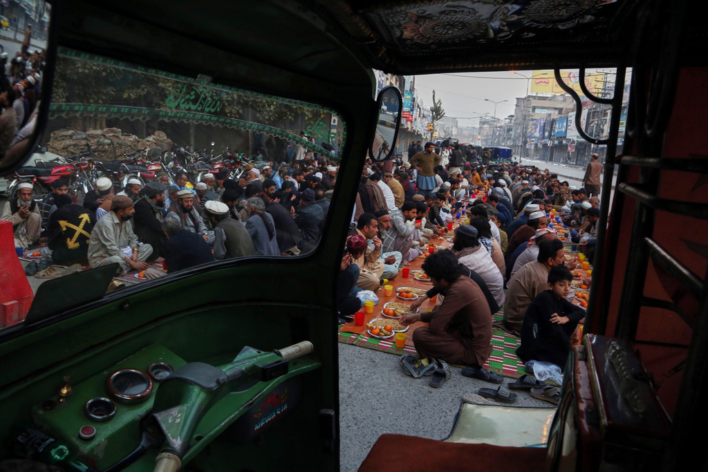 People eat food to break their fast during the Muslim holy fasting month of Ramadan, at a free food distribution point, seen through a rickshaw taxi in Peshawar, Pakistan, Thursday, Feb. 19, 2026. (AP Photo/Muhammad Sajjad)